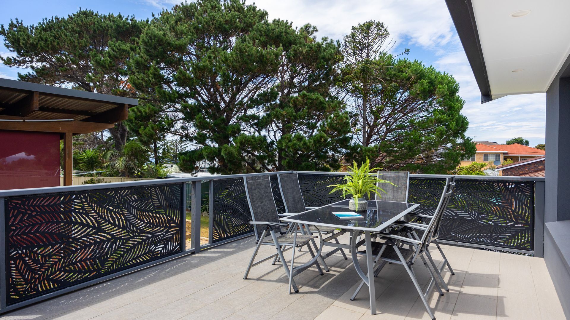 An outdoor patio with a table and chairs, surrounded by a decorative fence, and trees in the background.