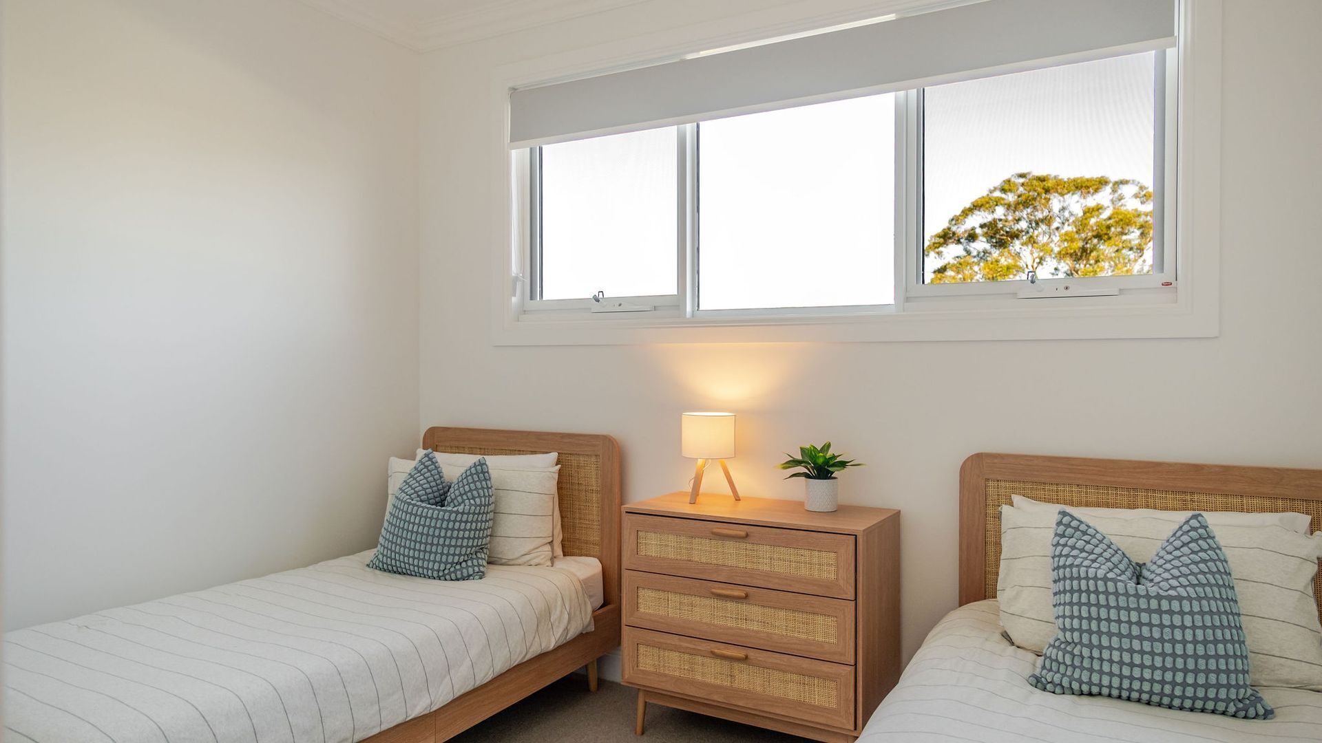 A bedroom with two single beds, a nightstand with a lamp, and a window with a view of trees.