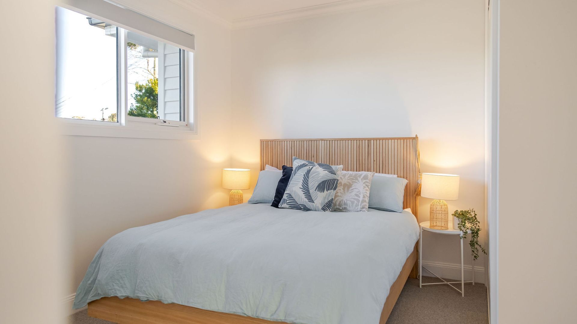 A bedroom with a bed, two bedside lamps, a window, and a bedside plant.