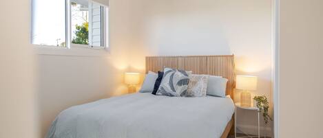 A bedroom with a bed, two bedside lamps, a window, and a bedside plant.