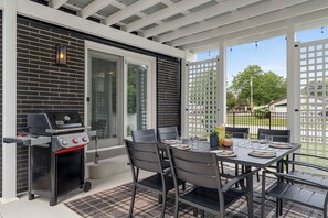 Un patio exterior con una parrilla, mesa dispuesta para cuatro y vistas del vecindario.