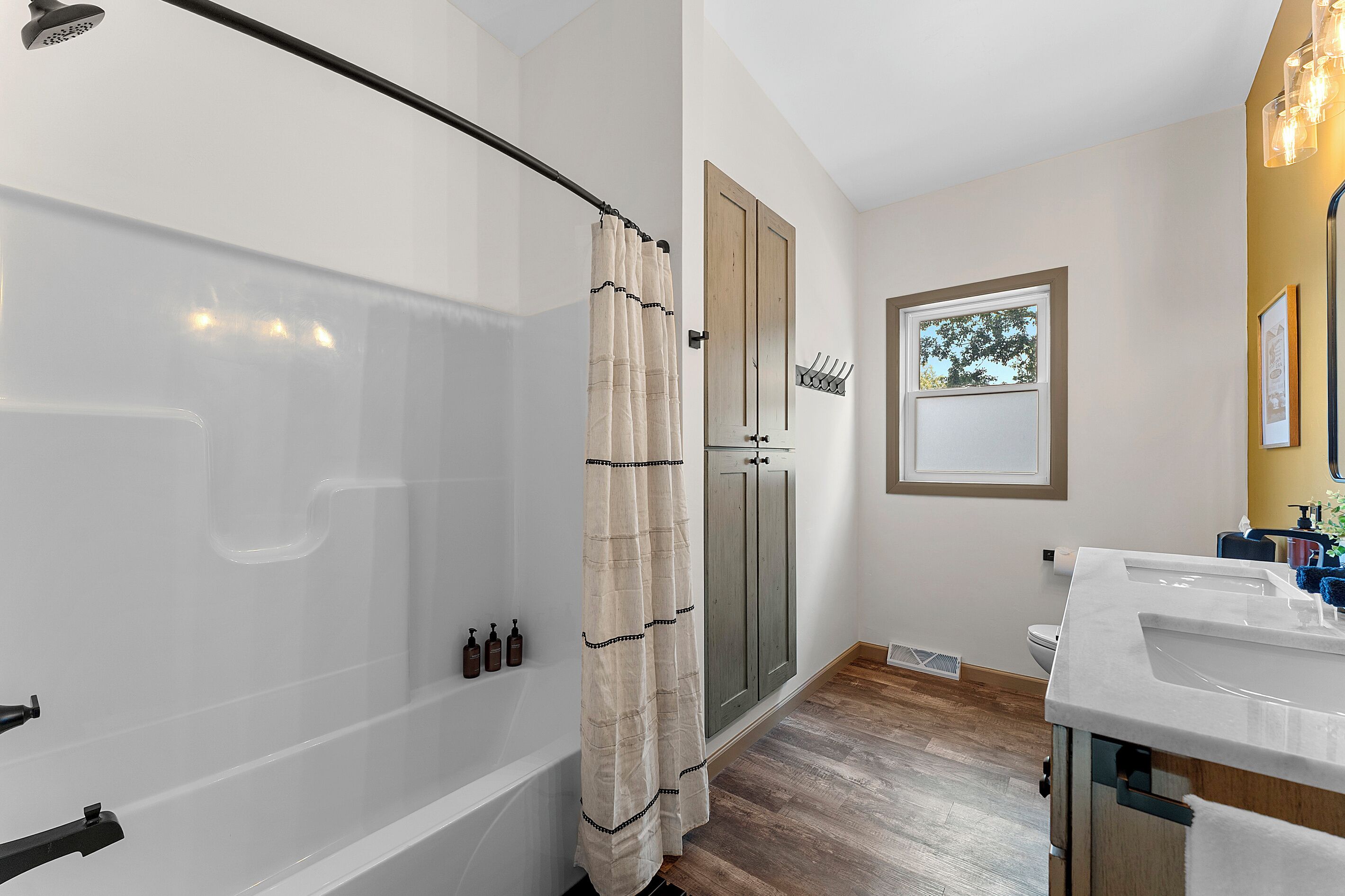 A bathroom with a shower, toilet, sink, and a window with a view of trees.