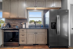 A kitchen with wooden cabinets, a stainless steel refrigerator, a built-in oven, and a window with a view of greenery.