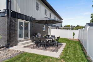 Een terras met een tafel, stoelen, een barbecue en een grote parasol.