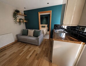 A modern apartment with a grey sofa, wooden flooring, a kitchen with black and white appliances, and teal walls. - Apartment Sleeps 4 - Town Centre & Near Beach (Newquay)