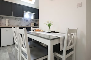 A modern kitchen with dark cabinets, a white countertop, and a small dining table with chairs. - Cosy One-Bedroom in Birchgrove, Cardiff (Cardiff)