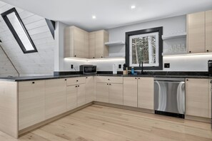 A modern kitchen with light wood cabinetry, a black countertop, a built-in microwave, and a dishwasher. - Modern A-Frame w/Sauna - Near Ragged Mtn, NH (Danbury)