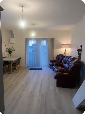 Ein Wohnzimmer mit braunem Ledersofa, einem Esstisch mit Stühlen und einer Lampe.