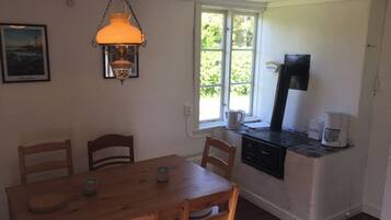A small kitchen with a wooden table and chairs, a coffee maker, and a window with a view of greenery.