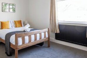 A bedroom with a wooden bed, a radiator, and a window with curtains. - 3 Br home perfect for big groups (Darlington)
