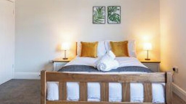 A hotel room with a wooden bed, two bedside lamps, and two wall-mounted pictures.