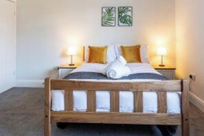 A hotel room with a wooden bed, two bedside lamps, and two wall-mounted pictures. - House - Sleeps 6 - Parking - Central Location (Darlington)