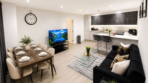 A modern living room with a dining area, a kitchen, and a TV. - North West London 3-Bed Flat, Sleeps 7 with Garden (London)