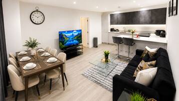 A modern living room with a dining area, a kitchen, and a TV.