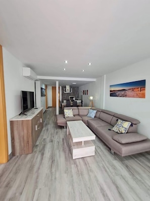 A modern living room with a sectional sofa, a coffee table, and a TV on a wooden cabinet. - Tenerife Paradise With Heated Pool (ADEJE)
