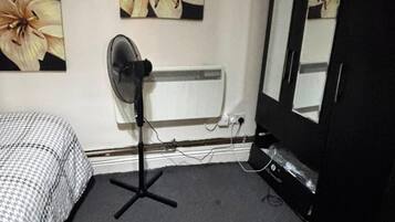 A room with a bed, a standing fan, a radiator, and a mirror.
