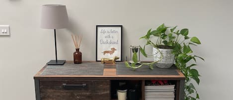 A wooden desk with drawers, a lamp, a framed quote, and a potted plant.