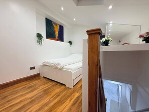 A bedroom with a bed, a painting on the wall, a potted plant, and a wooden floor. - Brand New! (Cardiff)