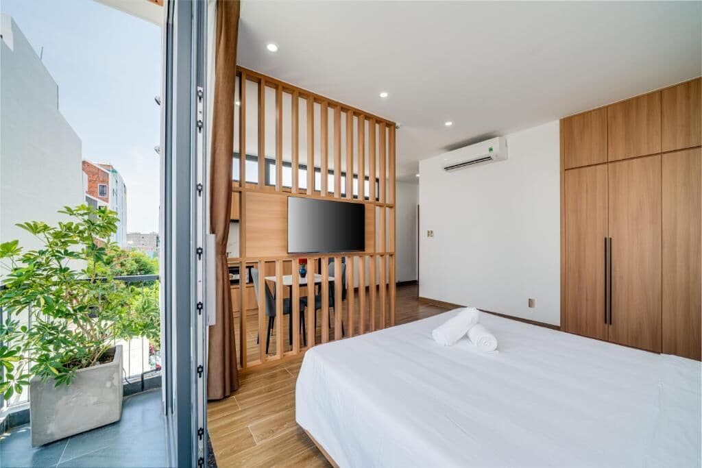 A modern hotel room with a bed, a TV, a wooden partition, and a balcony with a plant.