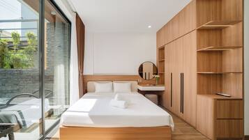A modern hotel room with a large bed, a wooden wardrobe, a bathroom with a mirror, and a view of greenery through a glass door.