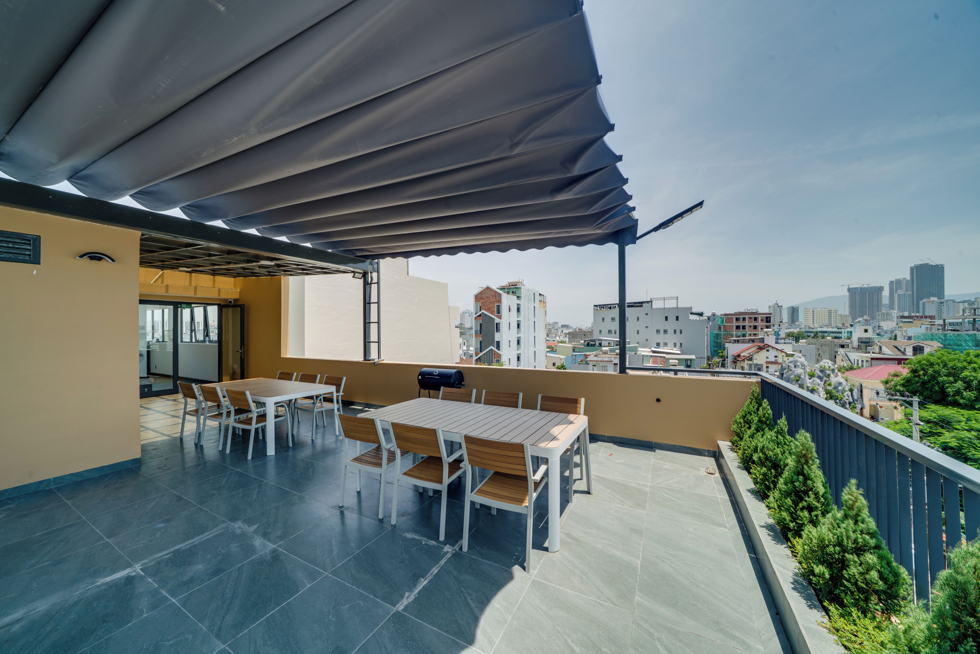 Um terraço ao ar livre com mesa, cadeiras, churrasqueira e vista para a cidade.