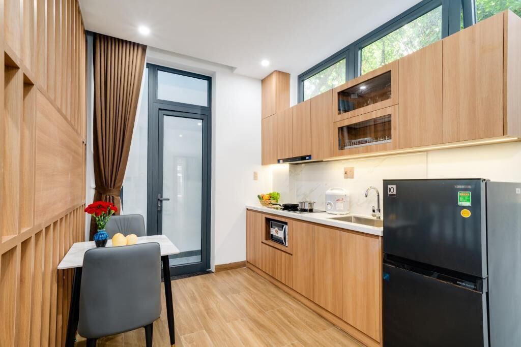 A compact kitchen with wooden cabinets, a black refrigerator, and a small dining table with a chair.