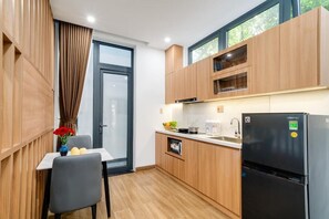 A compact kitchen with wooden cabinets, a black refrigerator, and a small dining table with a chair. - THE NEST Apartment - Self Checkin (An Hai)