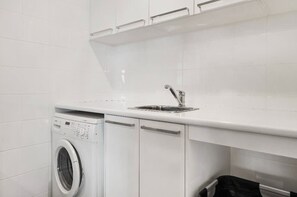Een kleine wasruimte met een wasmachine, een wasbak en een droogrek.