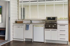 Een keuken met witte kasten, een inbouwoven, een vaatwasser en een raam met jaloezieën.