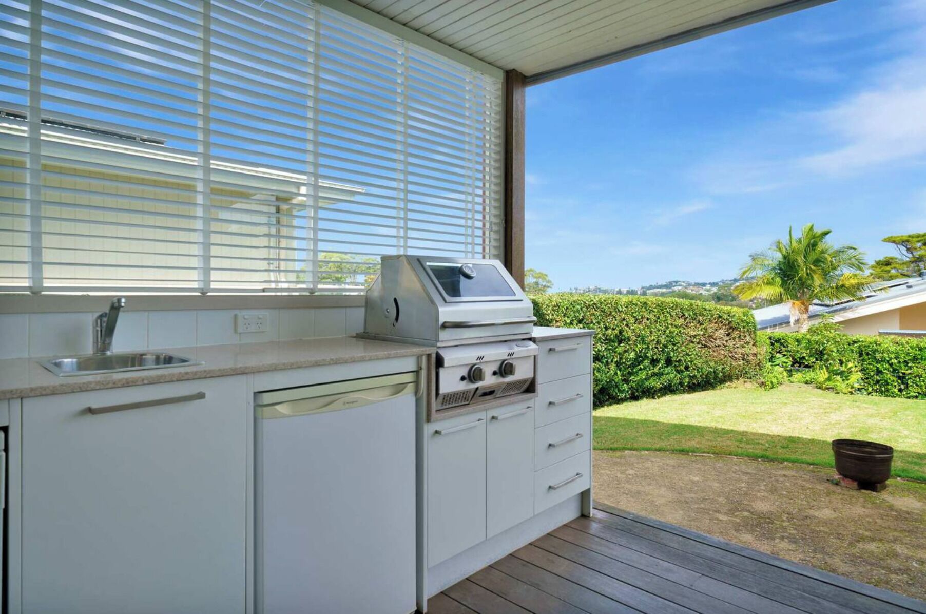 A kitchen with a built-in grill, a sink, and a window overlooking a garden.