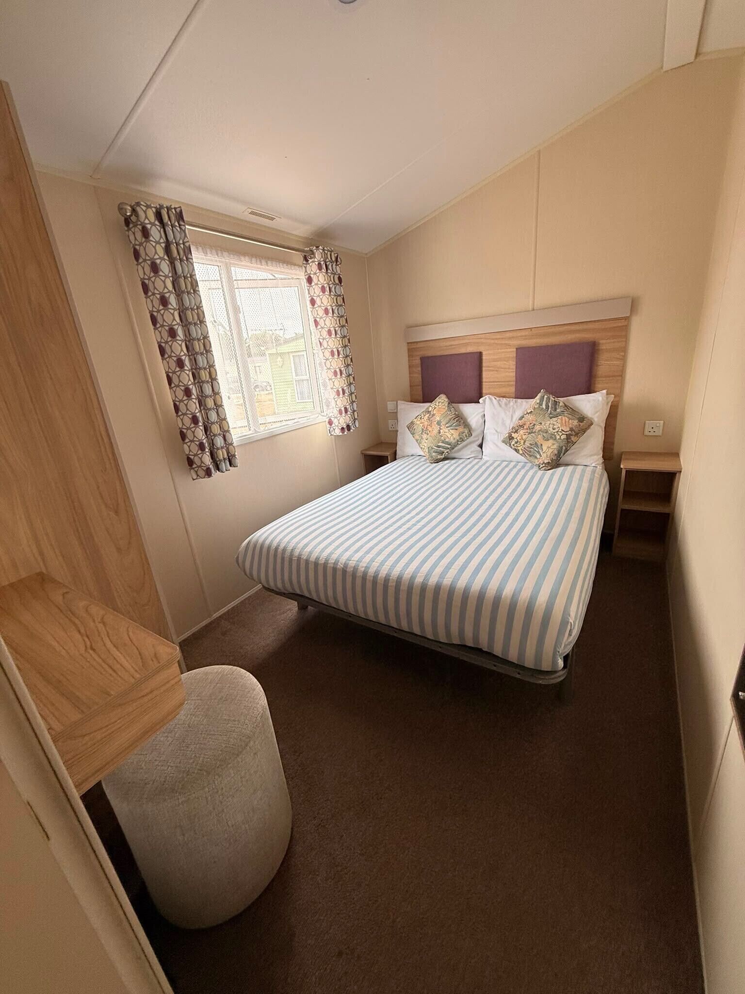 Een slaapkamer met een bed, een raam met behangetjes, een nachtkastje en een klein krukje.