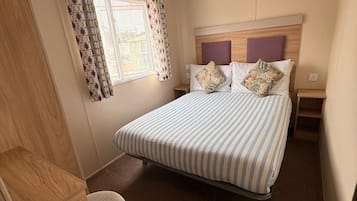 Een slaapkamer met een bed, een raam met behangetjes, een nachtkastje en een klein krukje.