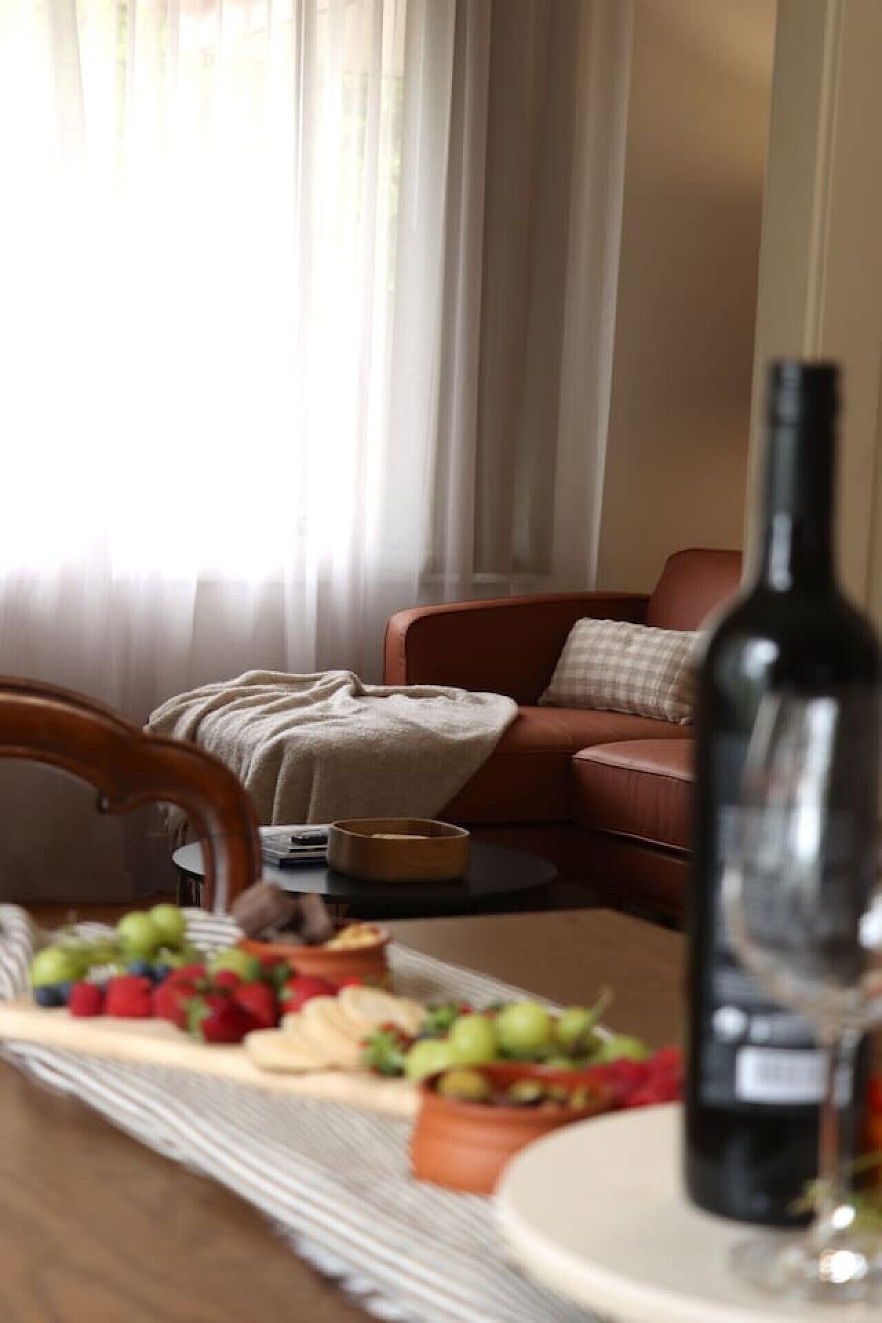 Een eettafel met een fles wijn, een glas en een schaal fruit.