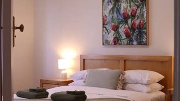 A bedroom with a wooden bed, a nightstand, a wall-mounted painting, and a ceiling fan.