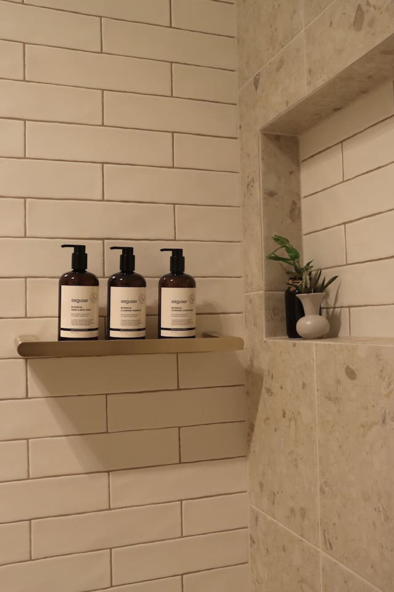 Una repisa con tres botellas de productos para el cuidado de la piel frente a una pared con diseño de ladrillo.