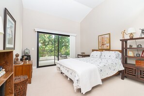 Ein Schlafzimmer mit Bett, Schreibtisch, Stuhl, Bücherregal und einer Schiebetür zum Balkon.