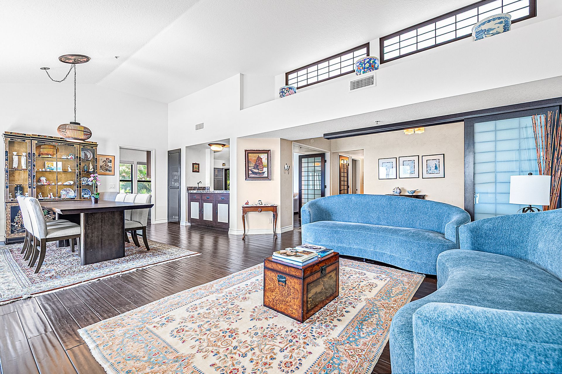 A spacious living room with a blue sofa, a wooden coffee table, and a dining area with a chandelier.