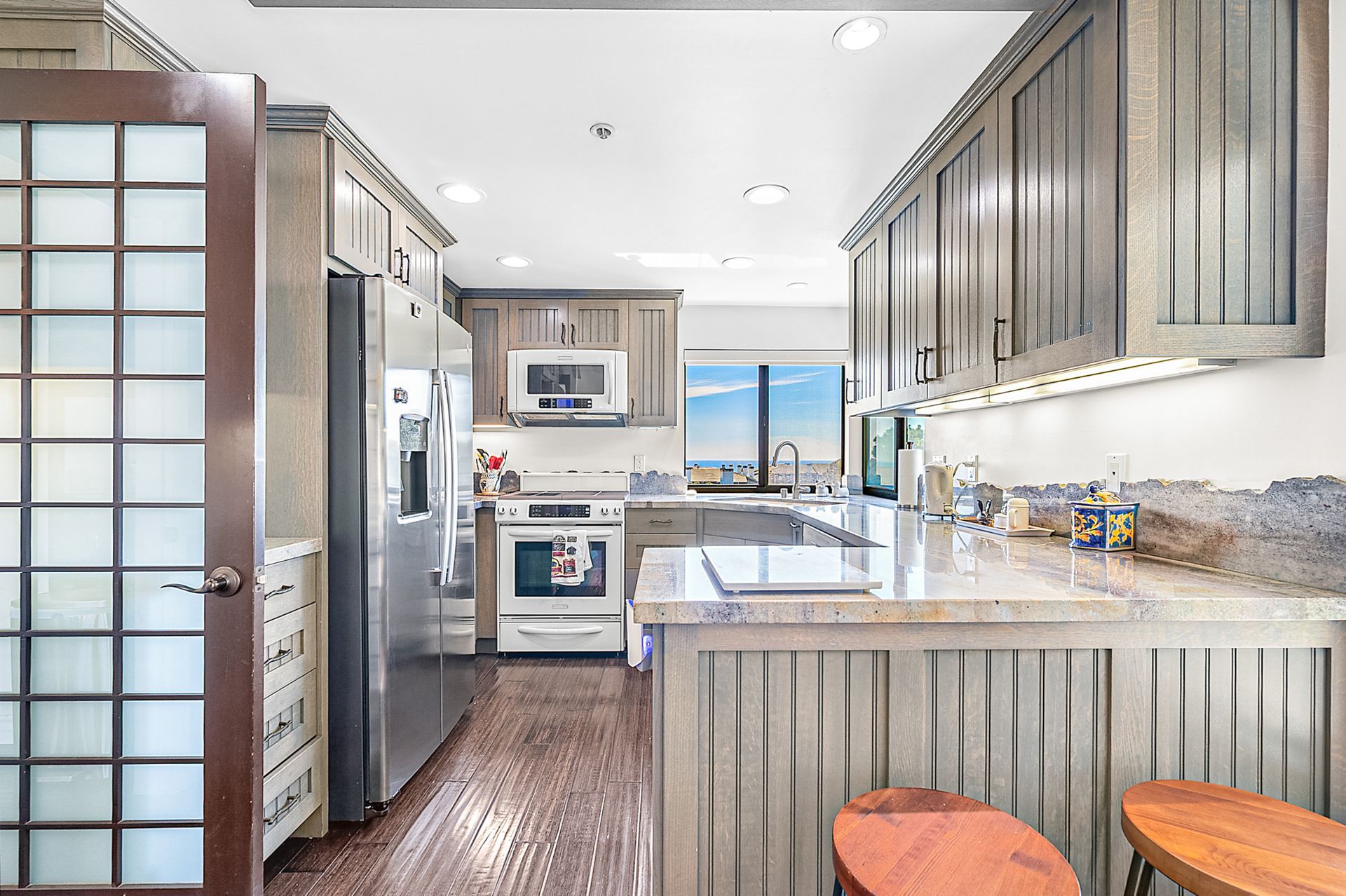A modern kitchen with a central island, stainless steel appliances, and a view through the window.