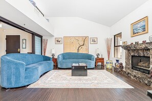 Ein Wohnzimmer mit zwei blauen Sesseln, einem Couchtisch, einem Kamin und Kunstwerken an den Wänden.