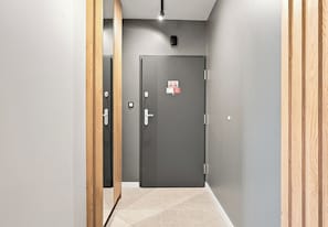 Un passadís amb una porta grisa al final, un interruptor de llum i un petit cartell a la porta.