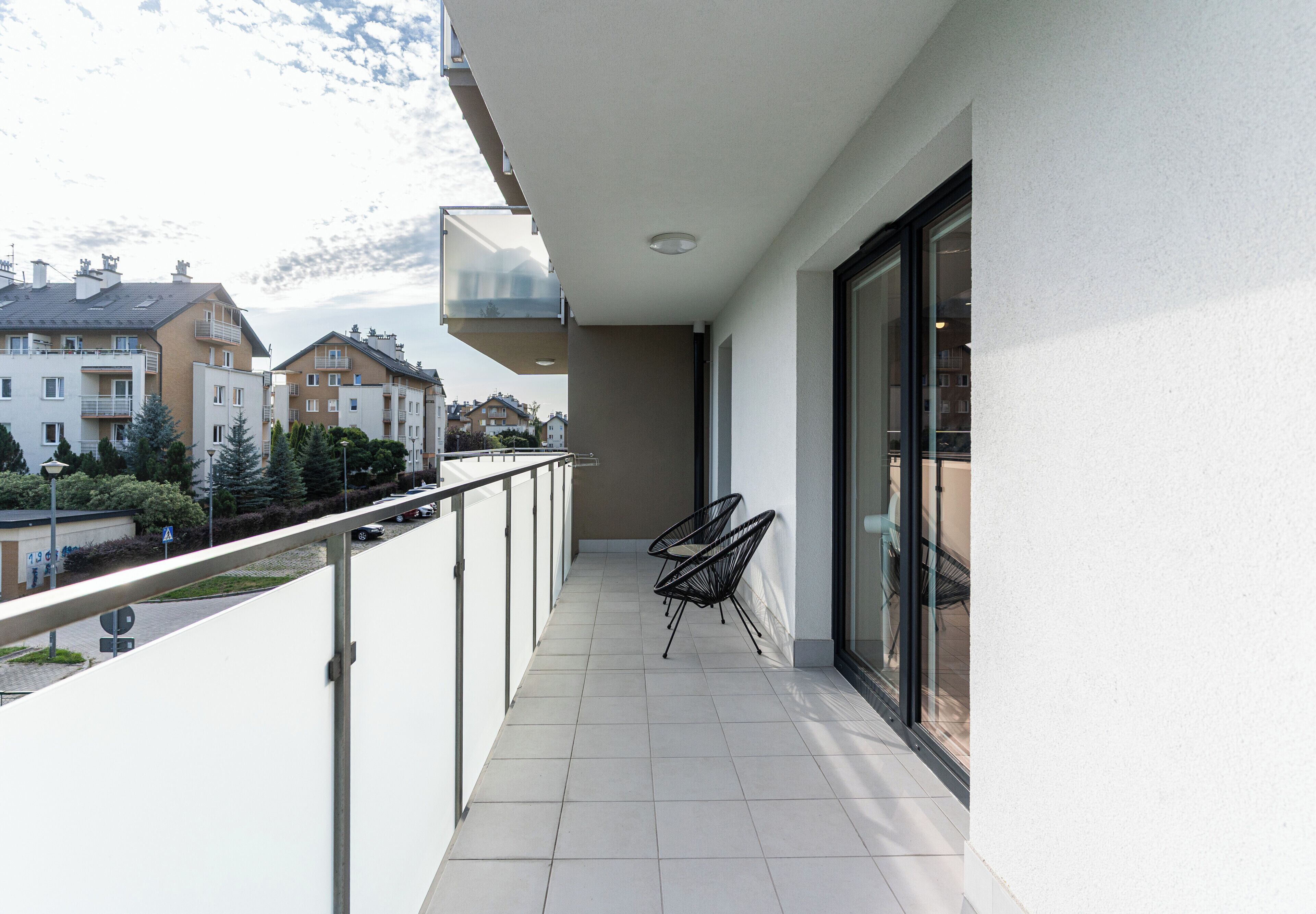 A balcony with a glass door, a metal railing, and two black chairs.