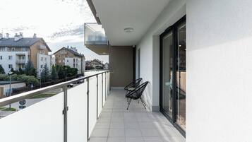 A balcony with a glass door, a metal railing, and two black chairs.