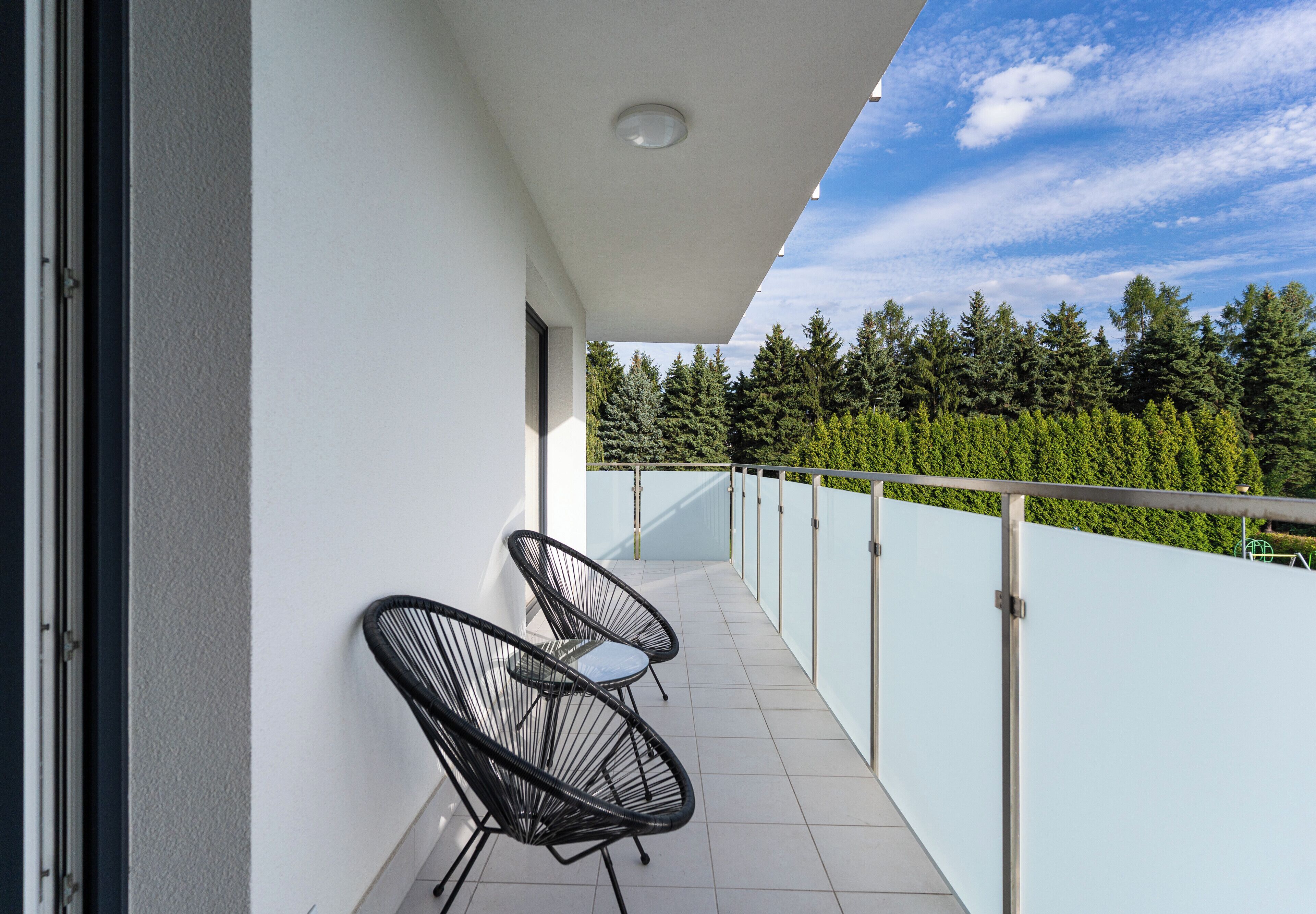 Un balcon avec deux chaises et une rambarde en verre donnant sur une zone boisée.