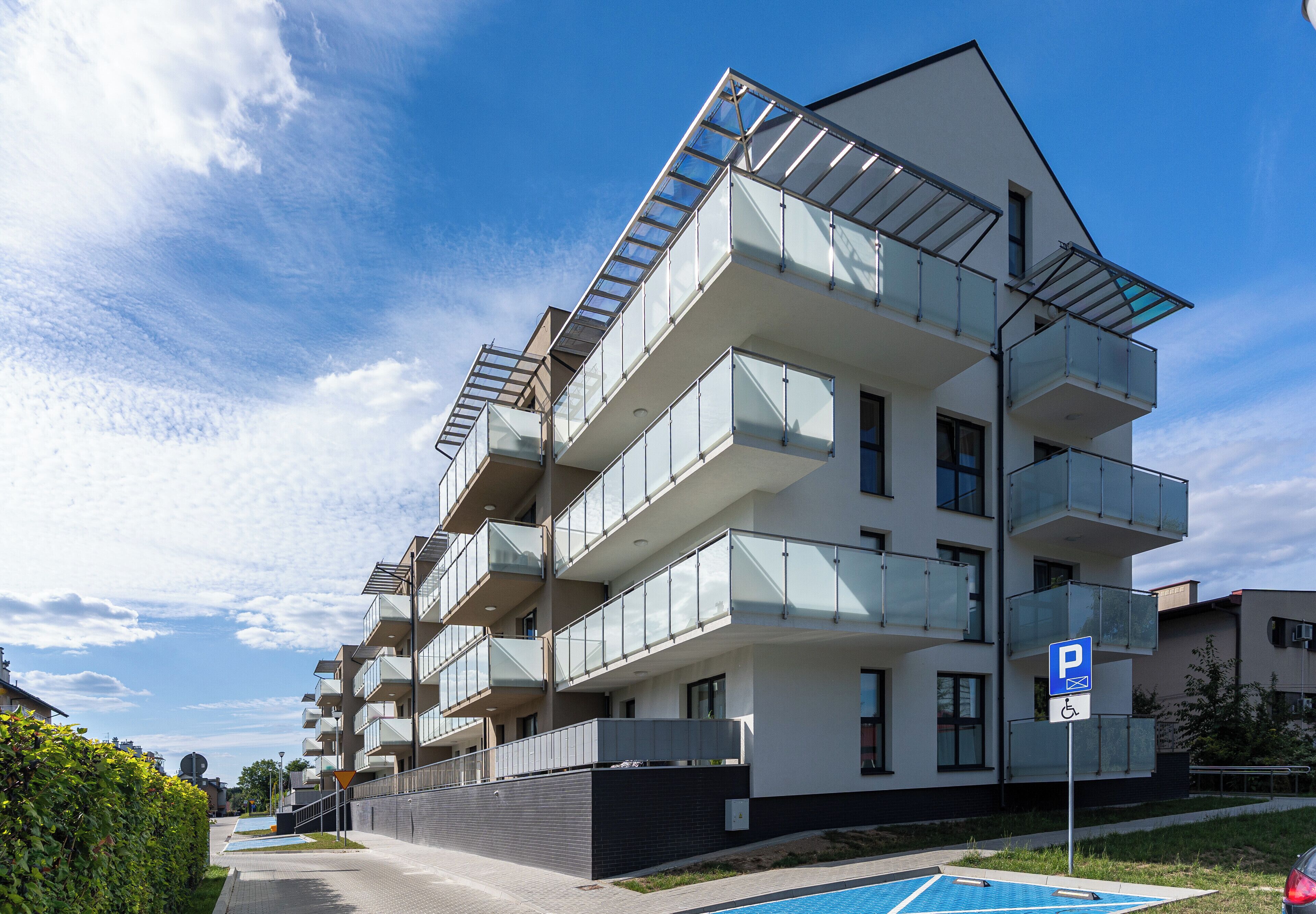 Ein modernes Mehrfamilienhaus mit Balkonen, einem Schwimmbad und einem Parkplatzschild.