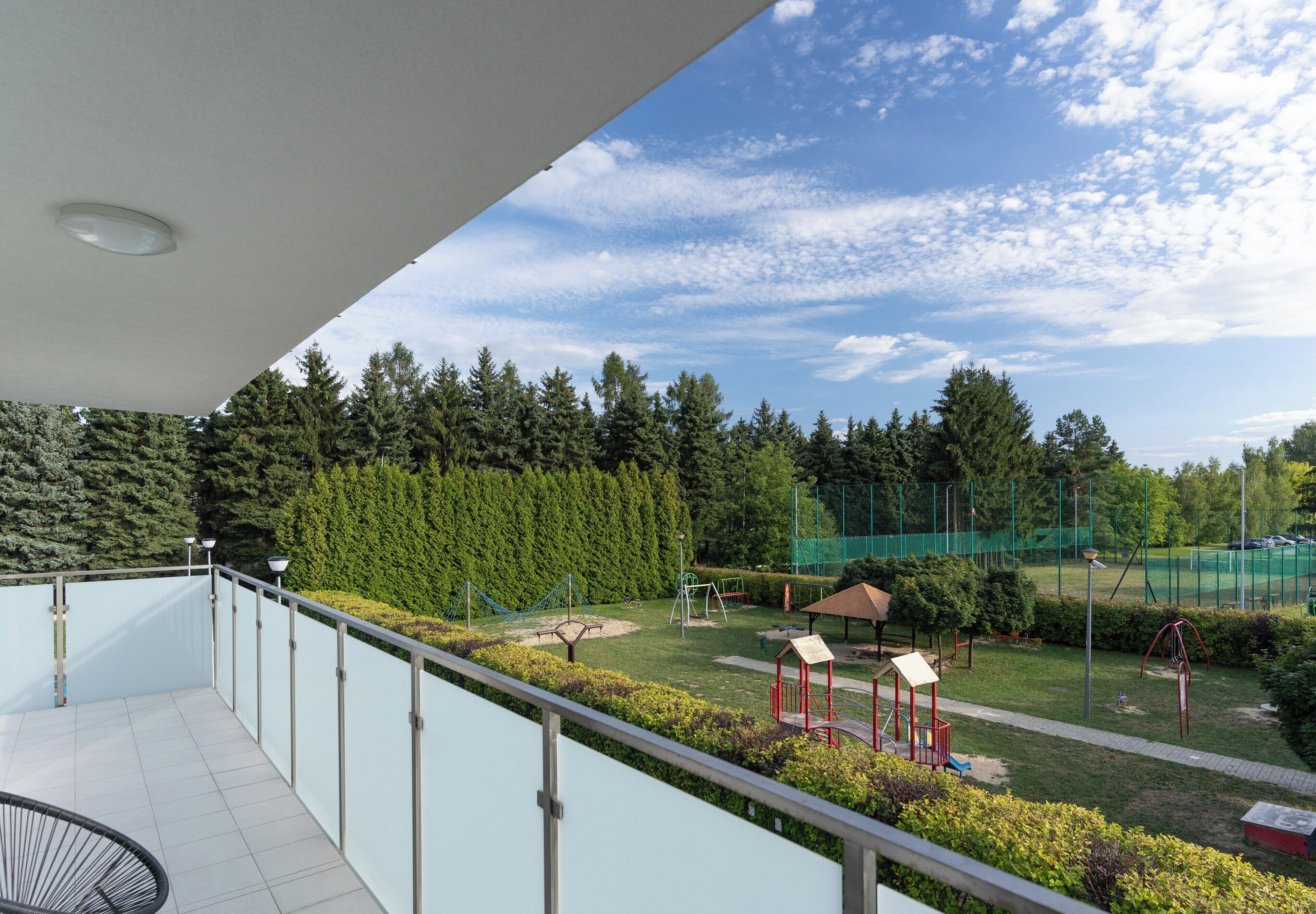 A balcony with a view of a park, including playground equipment and a sports field.