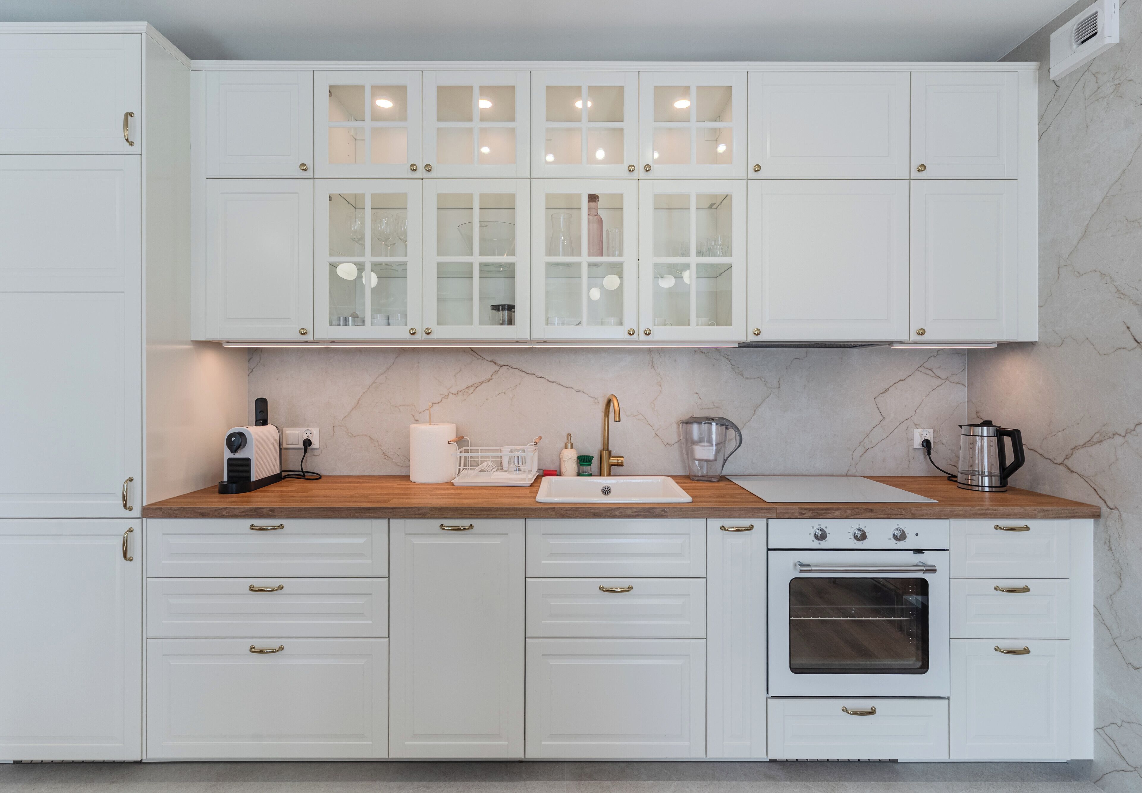 Una cocina con armarios blancos, un salpicadero de mármol, horno empotrado y encimera de madera.