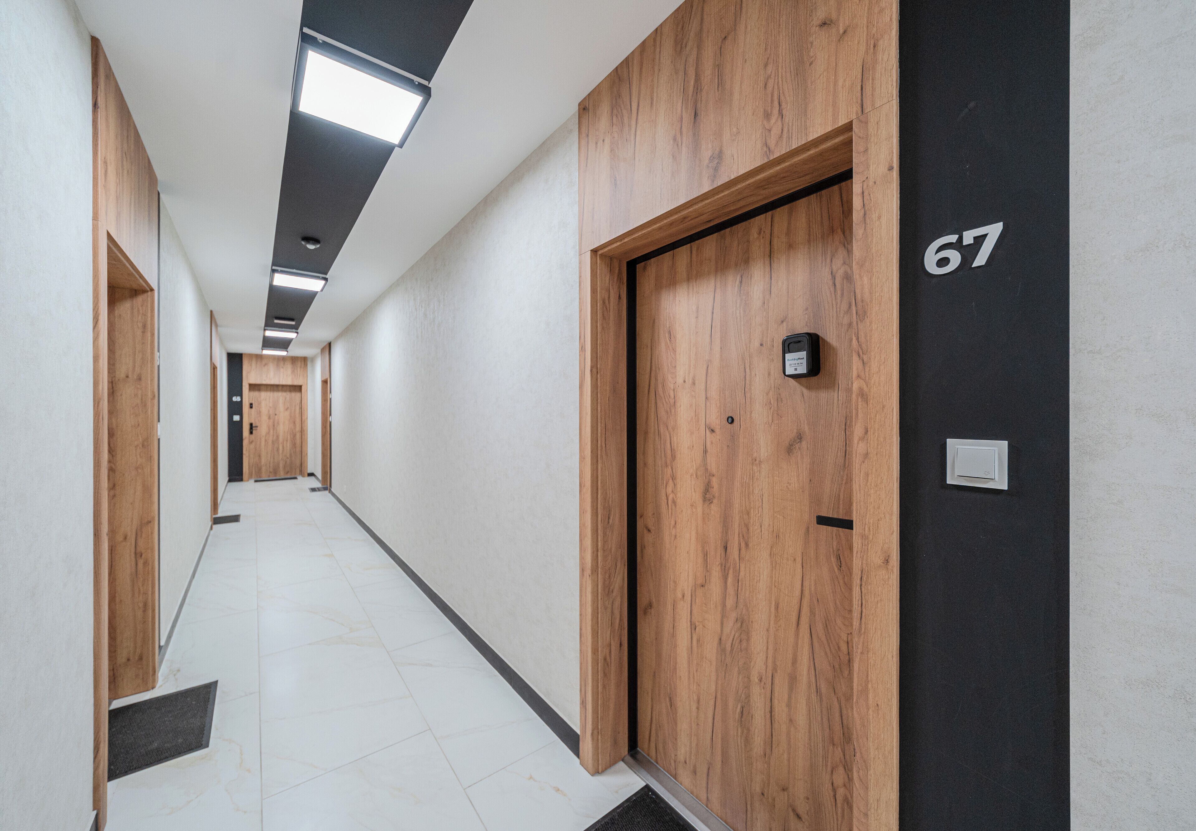 A hallway with wooden doors, a number 67 sign, and a light switch on the wall.