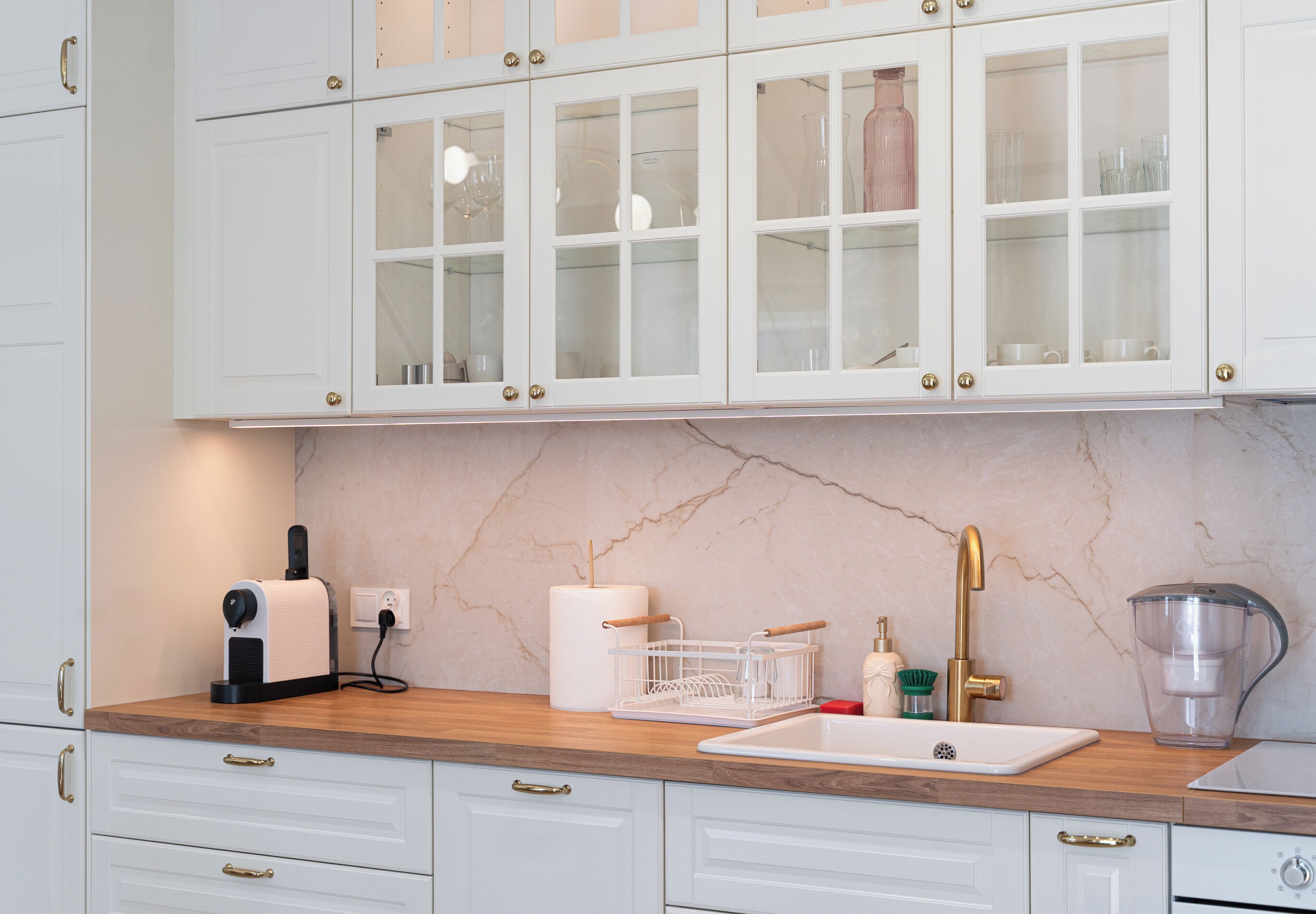 Cocina con armarios blancos, encimera de mármol, lavabo y cafetera.