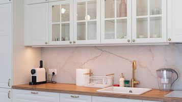 Cocina con armarios blancos, encimera de mármol, lavabo y cafetera.
