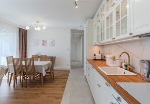 A modern kitchen with white cabinets, a wooden countertop, and a sink. - Podpromie Modern Apartment (Rzeszów)